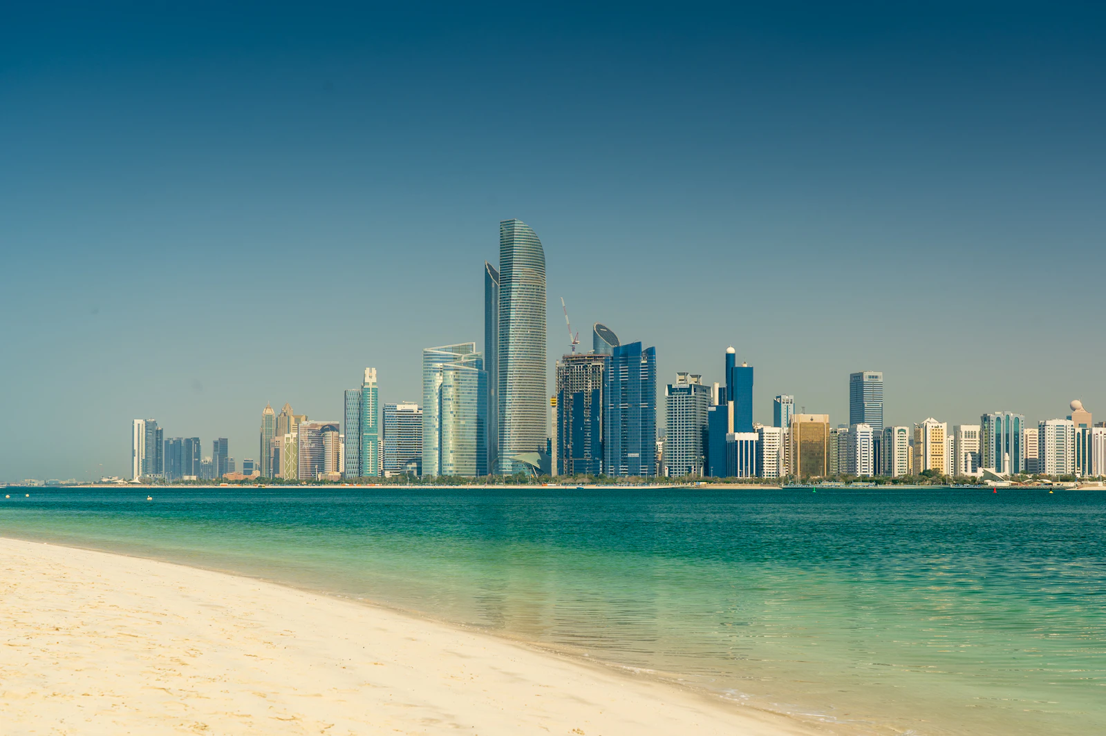The Abu Dhabi city skyline seen across calm water on a clear day.