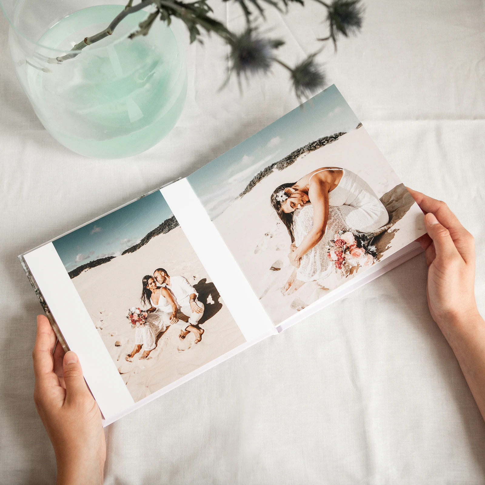 Hands holding an open wedding photo book, turning to printed photographs of a bride and groom.