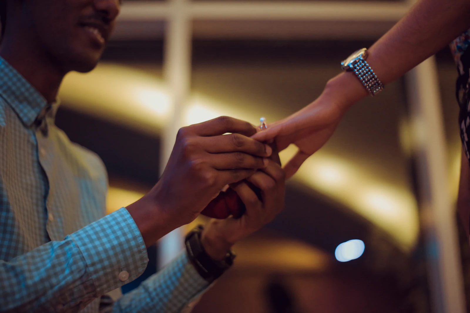 A man sliding an engagement ring onto a woman's hand against warm evening light.