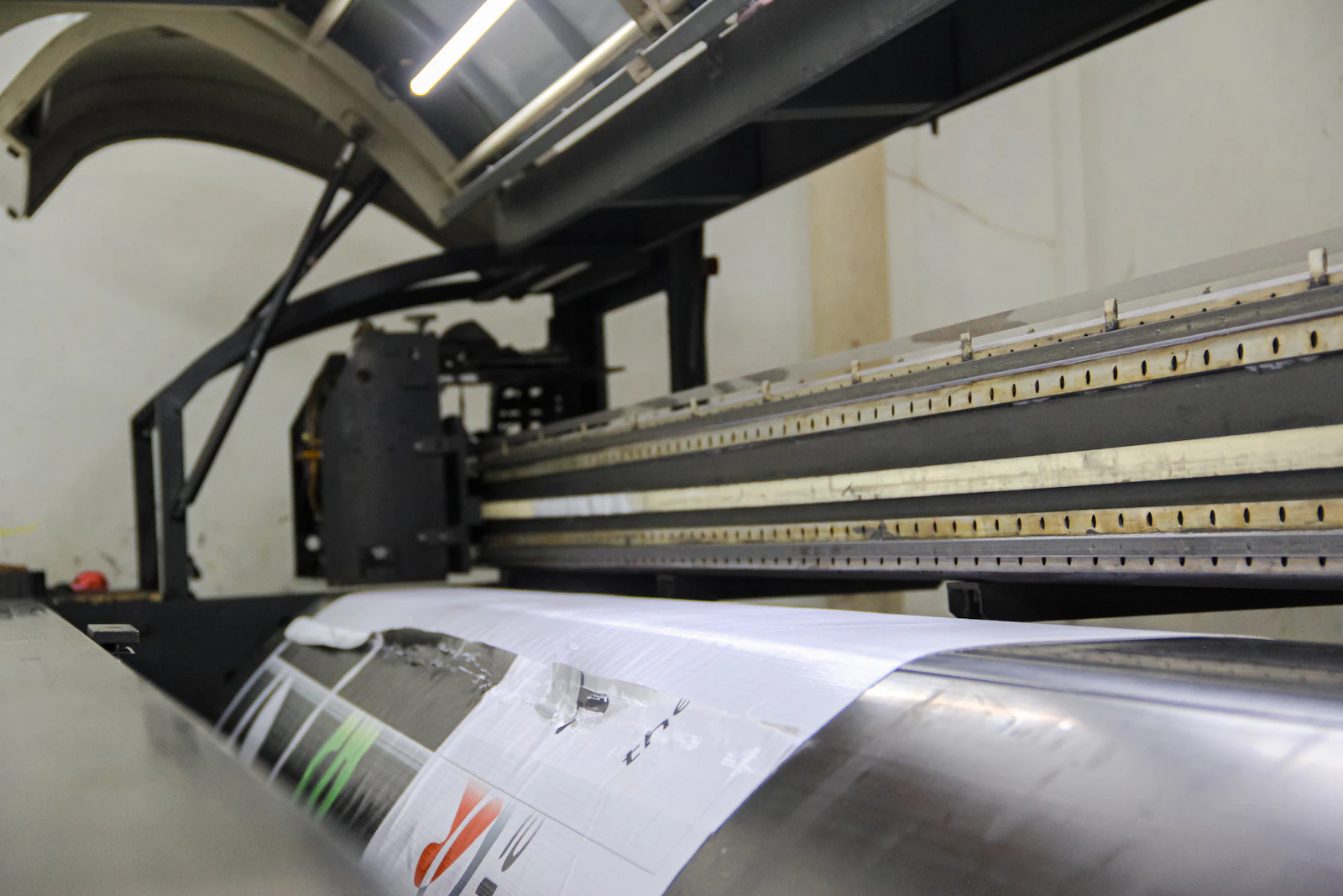 A large-format inkjet printer feeding a wide roll of paper.