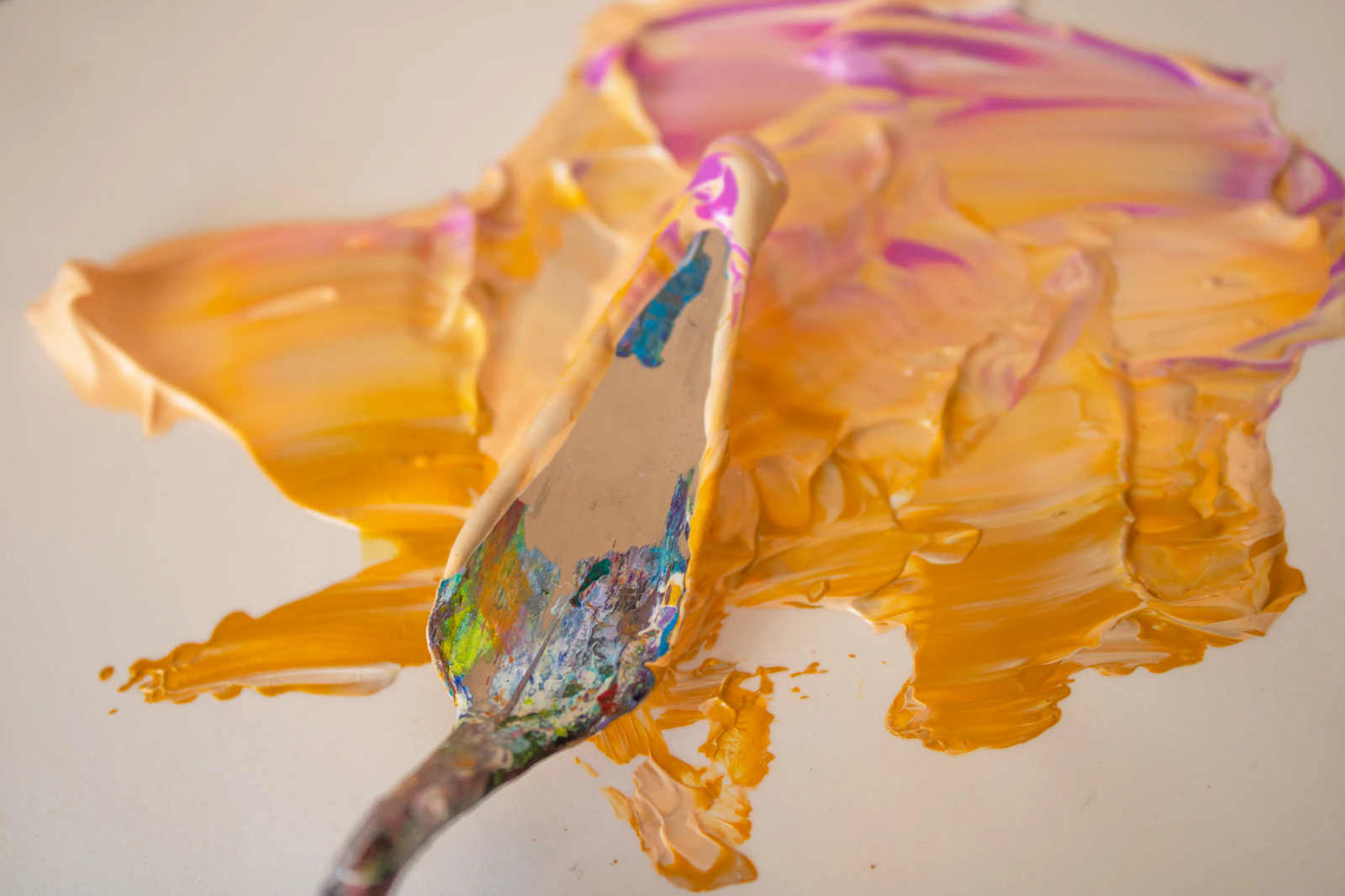A palette knife lifting thick amber paint, the ridges and relief clearly visible.