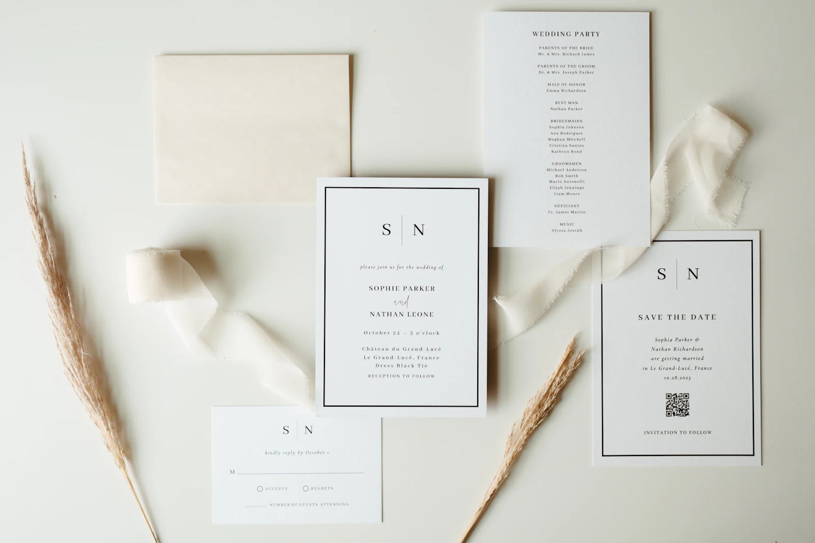 A wedding stationery suite laid flat on a pale surface: invitation, save the date card, RSVP, silk ribbon and dried grasses.