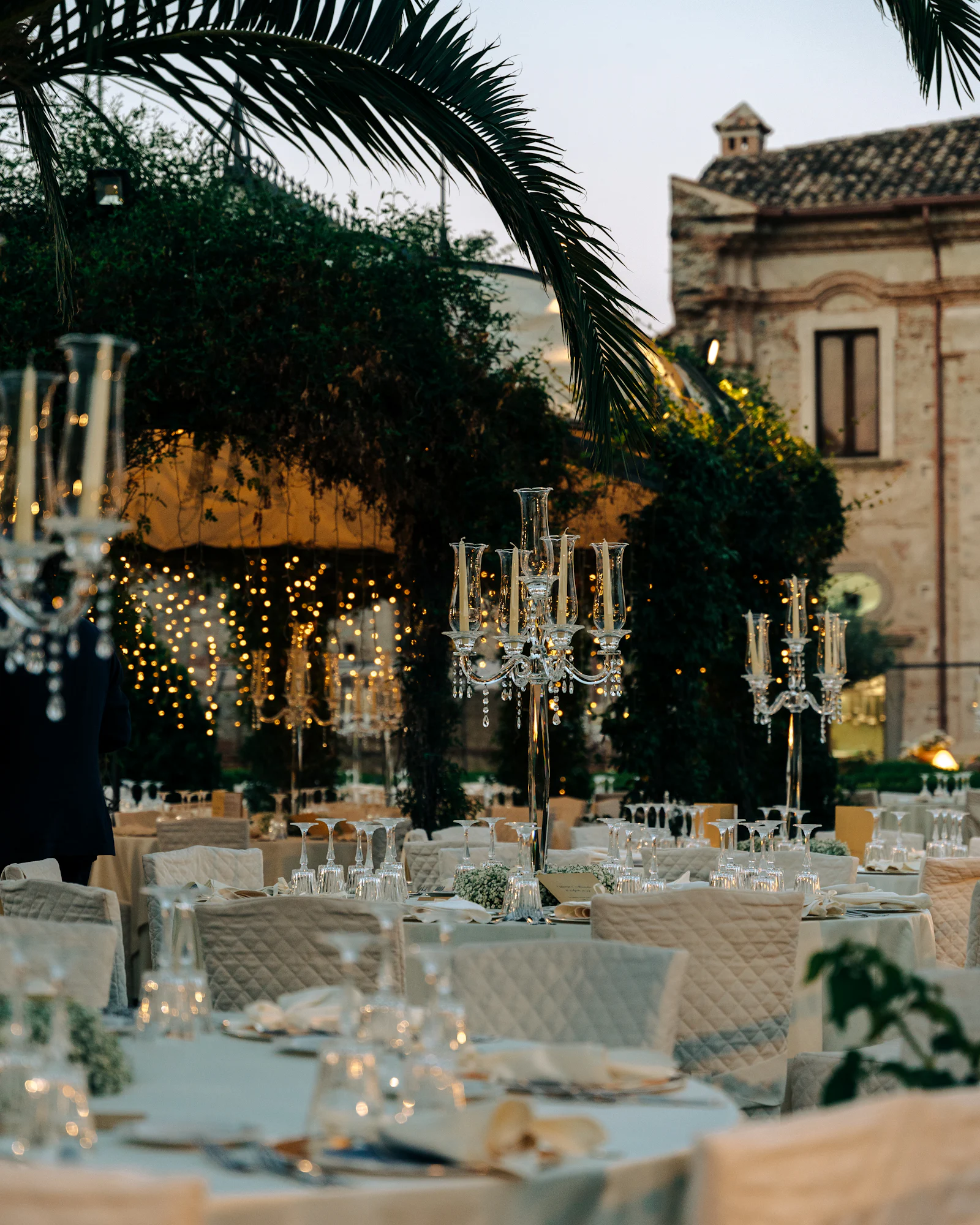 An elegant wedding reception table lit by candelabra and warm string lights in the evening.